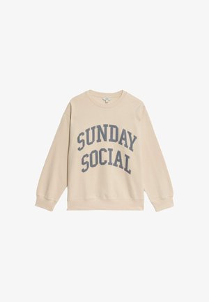 Beige sweatshirt with long sleeves and a crew neckline. Features "SUNDAY SOCIAL" text in dark gray across the front. Soft fabric.