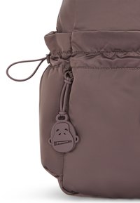 Sac à dos matelassé marron avec un cordon de serrage, orné d'une tirette de fermeture éclair en forme de visage de singe en caoutchouc et d'une texture lisse.