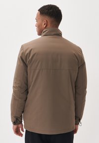 Giacca marrone, resistente all'acqua, con colletto alto, polsini elastici e una texture liscia. Presenta un design semplice e pulito senza loghi visibili.