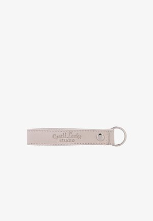 Beiger Leder-Schlüsselanhänger mit einem silbernen Metallring und "Gusti Leder studio" auf dem Lederband graviert.