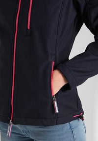 Granatowa kurtka z różowymi suwakami, dwoma bocznymi kieszeniami, elastycznym ściągaczem u dołu i teksturowaną tkaniną. Minimalistyczny design.