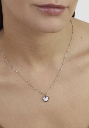 Silberne Halskette mit einer kleinen, herzförmigen Anhänger, der eine glatte, reflektierende Oberfläche und einen kontrastierenden dunklen Rand aufweist.