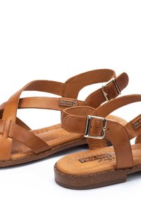 Sandales en cuir marron avec des brides croisées et des boucles ajustables, dotées d'une semelle intérieure rembourrée et d'une semelle extérieure texturée pour une meilleure adhérence.