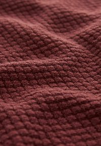 Tissu bordeaux texturé avec un petit motif carré en relief, présentant une texture douce et des plis délicats. Convient pour les textiles ou la tapisserie.