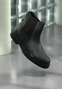 Black leather ankle boots with elastic side panels, round toe, and flat rubber sole. Features a small logo on the side.