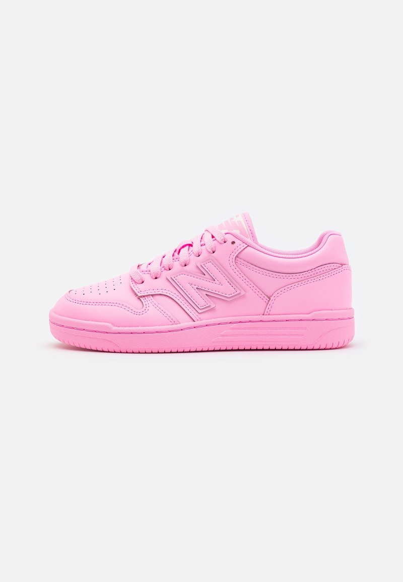 Baskets basses de sport rose uni avec laçage sur le devant, perforations au niveau des orteils et un grand logo "N" sur le côté.