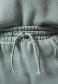 Pantalon de survêtement bleu clair avec une taille à cordon de serrage à texture froncée et des cordons tressés, fabriqué en tissu doux.