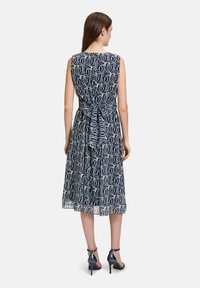 Námornícky bezrukávový šaty s bielym kruhovým vzorom, sťahovaným pásom a detailom na viazanie, splývavá látka, sukňa po kolená, doplnené čiernymi podpätkami.