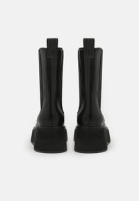 Stivaletti neri lucidi alla caviglia con suola platform spessa, caratterizzati da una texture liscia e uno stivale alto e dritto. Cuciture di rinforzo lungo i lati.