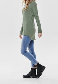 Grön långärmad topp med sidoflikar, kombinerad med ljusblå slim fit-jeans och svarta snörade ankboots med en robust sula.