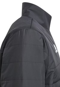 Doudoune noire avec un col haut, présentant des sections matelassées, une texture lisse et un logo Adidas blanc sur la poitrine.