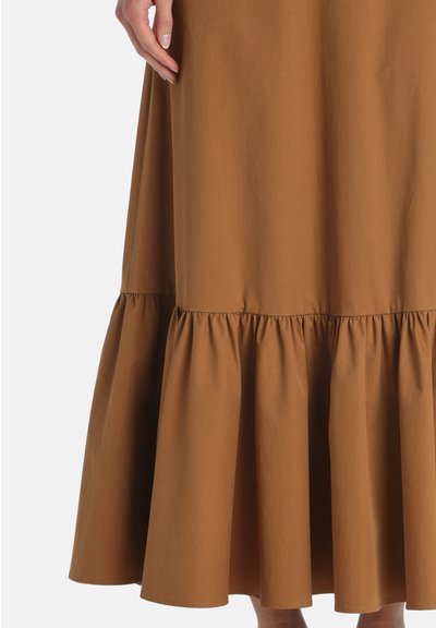 Brown tiered skirt with ruffled hem worn by a person with hand resting lightly on the side, set against a white background.