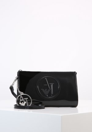 Musta kiiltävä ranteeseen sopiva laukku, jossa on prässätty pyöreä AJ-logo ja siihen sopiva metallinen AJ-avaimenperä valkoisella pinnalla valkoista taustaa vasten.