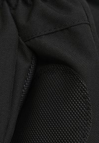 Nahaufnahme eines schwarzen strukturierten Stoffes mit verstärktem, gepolstertem Ellbogenpatch, der ein rautenförmiges Griffmuster und detaillierte Nähte aufweist.