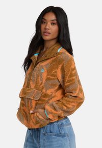 Fleecejack in oranje en bruin met een patroonontwerp, voorzien van een drukknopenkraag, een verstelbare zoom en een voorzak.