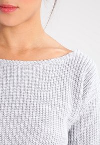 Jasnoszary sweter dzianinowy o prążkowanej strukturze, szerokim dekolcie i lekko opadających ramionach, ukazujący miękki, komfortowy materiał.
