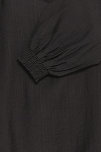 Indumento nero con maniche a sbuffo in tessuto strutturato e polsino elasticizzato, che mostra un aspetto morbido e drappeggiato.