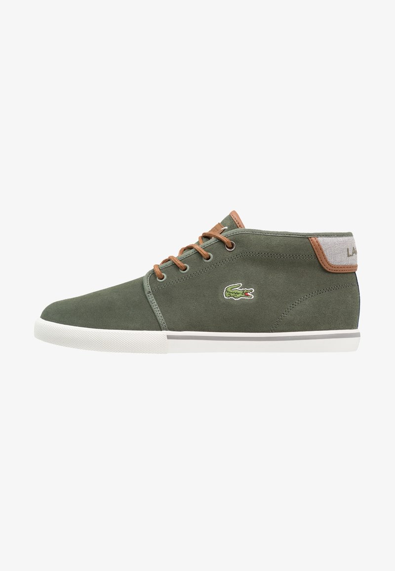 Baskets basses en suède vert avec lacets marron, semelle en caoutchouc blanche et logo crocodile vert brodé sur le côté.
