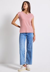 Růžové tričko s krátkým rukávem a výstřihem do V, zdobené švy, v kombinaci s světlými modrými volnými džínami a béžovými teniskami s růžovými akcenty.
