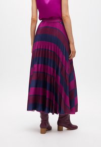 Gonna maxi a pieghe in rosa scuro e righe blu navy, con una texture fluida, indossata con stivali borgogna al ginocchio. La gonna ha una vita aderente.