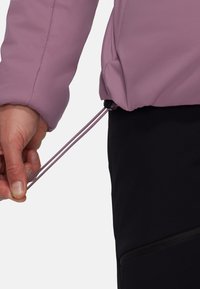 Fialová zateplená bunda s elastickým sťahovaním na spodnom okraji, kombinovaná s čiernymi nohavicami s vreckom na zips, zobrazená v pozícii nastavovania rukou.