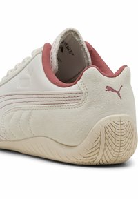 Zapatilla blanca con suela de goma rosa y detalles en ante. Presenta un patrón texturizado a lo largo del costado y un collar acolchado para mayor comodidad.