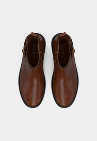 Rudos odinės aulinukai iki kulkšnies su lygiu paviršiumi, apvaliu nosiu, juodu padu ir auksiniais akcentais. Sukurti su plyšiais, kad būtų lengva dėvėti.