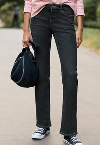 Czarne jeansy straight-leg z wysokim stanem, zestawione z różowym swetrem i czarną torbą na ramię z metalowymi akcentami w kolorze srebrnym oraz teksturowanym wykończeniem.