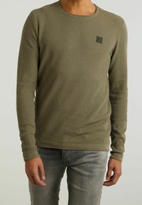 Oliwkowa sweter z długim rękawem o teksturowanym wzorze, okrągłym dekolcie i małej naszywce z logo na piersi. Rybkowany dół.