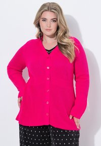 Sweter dzianinowy w intensywnym różowym kolorze z dekoltem w serek, długimi rękawami i guzikami z przodu. Posiada teksturowaną tkaninę oraz boczne kieszenie.