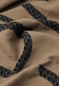 Brunt stof med en blød tekstur prydes af et sort geometrisk mønster med overlappende former og diamantdesigns, hvilket skaber visuel interesse.