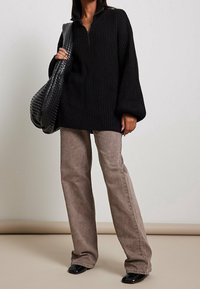 Schwarzer, gerippter Strickpullover mit halbem Reißverschluss, kombiniert mit hellbraunen, weiten Hosen und einer strukturierten schwarzen Schultertasche. Schwarze Schuhe.