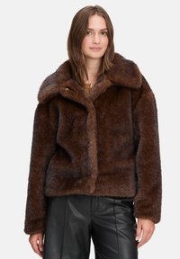 Brun faux fur jakke med en stor krave, blød tekstur og tætsiddende design. Har knaplukning og lange ærmer. Båret med sorte bukser.