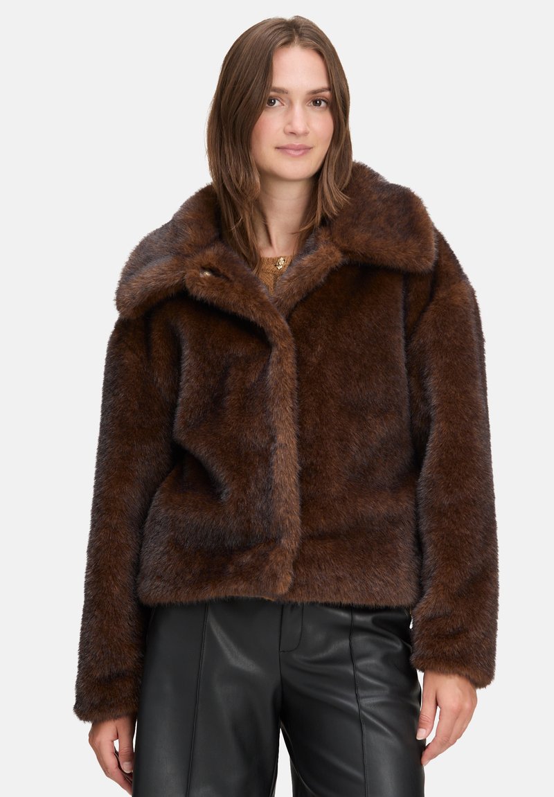 Brun faux fur jakke med en stor krave, blød tekstur og tætsiddende design. Har knaplukning og lange ærmer. Båret med sorte bukser.