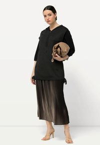 Tunika nera in maglia con cerniera completa e lacci laterali, abbinata a una lunga gonna plissettata in toni di marrone sfumati. Include tacchi beige con lacci.
