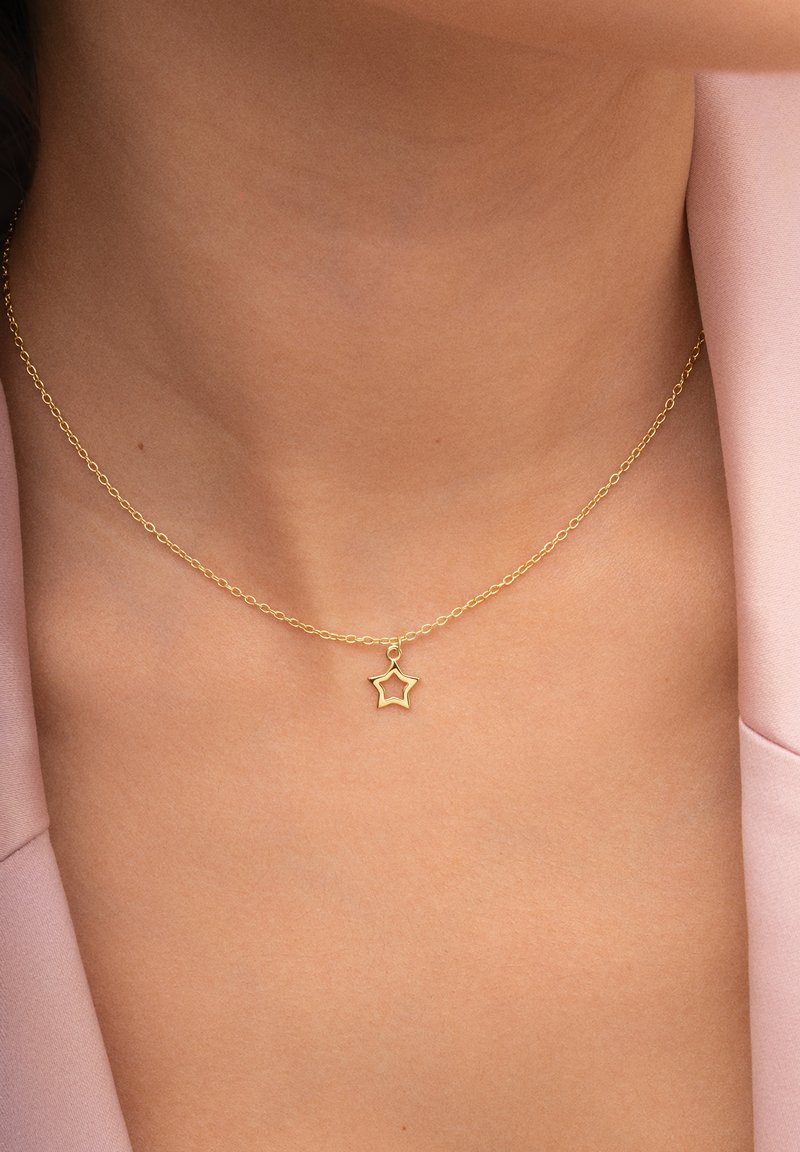Gouden ketting met een kleine sterpendant, op een blote nek tegen een roze stoffen achtergrond. Eenvoudig ontwerp en gladde textuur.