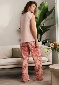Haut rose ample avec des manches courtes associé à un pantalon à motif floral dans des tons de rose et de rouge. Tissu texturé avec un design décontracté.