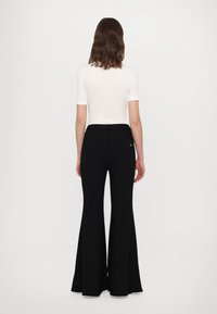 Black flared trousers with a fitted waist, made from a smooth fabric. Features back pockets and a subtle logo detail on the right rear.