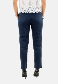Pantaloni tailored blu navy con una vestibilità slim, dotati di due tasche posteriori e una texture liscia. Indossati con scarpe con tacco nere.