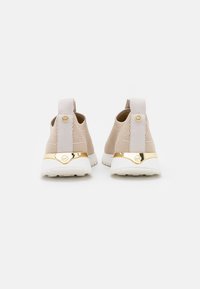 Sneakers in maglia beige con una finitura metallica dorata e suola bianca. Parte superiore in tessuto morbido con una linguetta sul retro per facilitarne l'indossamento.