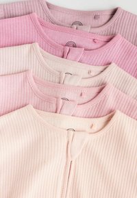 Cinq hauts en tricot côtelé dans des teintes de rose et de beige, empilés et alignés par leurs encolures rondes avec des étiquettes en tissu visibles.