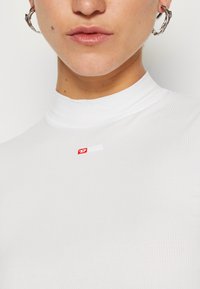 White ribbed turtleneck top featuring a small red "Diesel" logo on the chest. Fitted design with smooth texture and high neckline.