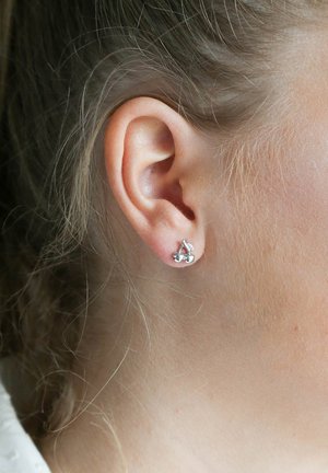 Silberne kirschförmige Ohrringe mit zwei kleinen Kugeln und einem Blattakzent, vor einem hellen Teint und lockigem Haar.