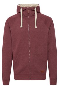 Maroon zip-up hoodie with a cream interior. Features a drawstring hood, front pockets, ribbed cuffs, and a leather logo patch. Soft fabric texture.