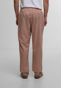 Pantaloni rayati în roșu și bej, cu o talie elastică, picioare drepte și o textură fină. Încălțăminte casual completează aspectul.