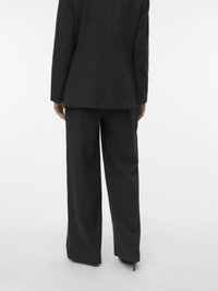 Temno siv po meri krojen kostim z dolgim srajčnim suknjičem in širokimi hlačnicami. Gladek material z rahlo teksturo, minimalističen dizajn brez vidnih detajlov.