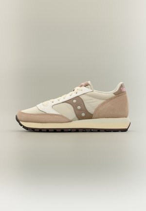 Μπεζ και λευκό αθλητικό παπούτσι Saucony με σουέντ και δερμάτινες επενδύσεις, κλείσιμο με κορδόνια και μαύρη λαστιχένια σόλα σε ουδέτερο φόντο.