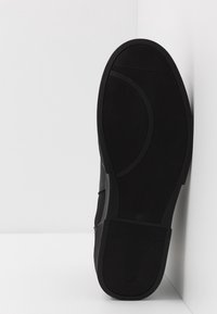 Černá teniska s texturovanou gumovou podrážkou, o zakřiveném profilu, hladkým svrchním materiálem a elegantním designem. Bez viditelných tkaniček nebo kovových částí.