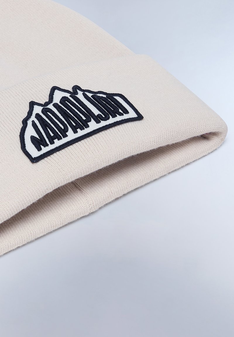 Berretto a maglia beige con un'etichetta ricamata nera raffigurante un design montano e testo. Texture morbida con un risvolto.