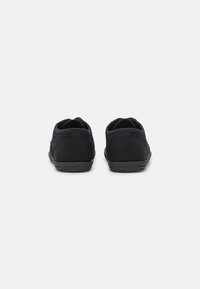 Ein Paar schwarze lässige Slipschuhe von hinten auf einem weißen Hintergrund, mit Stoff- und Gummisohlen.
